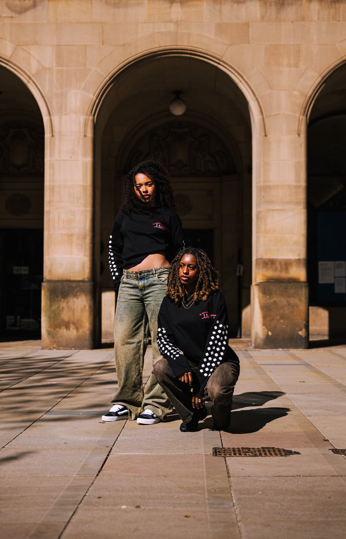 Two models wearing the original black Clover longsleeve outside a stone archway